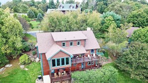 Uma casa grande de dois andares, com varanda e um deck, rodeada por muita vegetação.