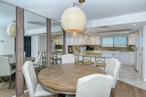 A modern kitchen with white cabinets, a large island, and a dining area with a round table and chairs.