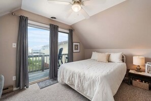Et soveværelse med seng, natbord, lampe, loftventilator og udsigt ud.