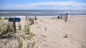 Una playa arenosa con una valla de madera y un cartel azul.
