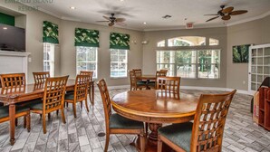 Un comedor con una mesa redonda de madera y sillas, ventiladores de techo y ventanas grandes con persianas.