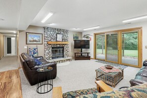 Ein Wohnzimmer mit Kamin aus Stein, Ledersofas, einem Flachbildfernseher und einer großen Schiebeglastür, die auf eine Terrasse führt.