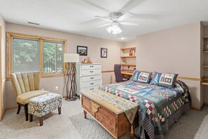 Ein Schlafzimmer mit einem Bett, einem Sessel, einem Schminktisch, einem Schreibtisch, einer Lampe und einem Deckenventilator.