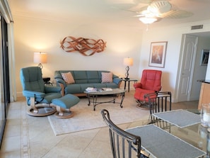 A living room with a sectional sofa, a rocking chair, a glass coffee table, and a dining table with chairs.