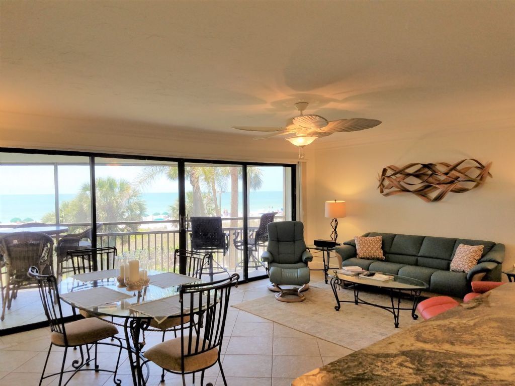 A living room with a balcony, a ceiling fan, and a view of the ocean.