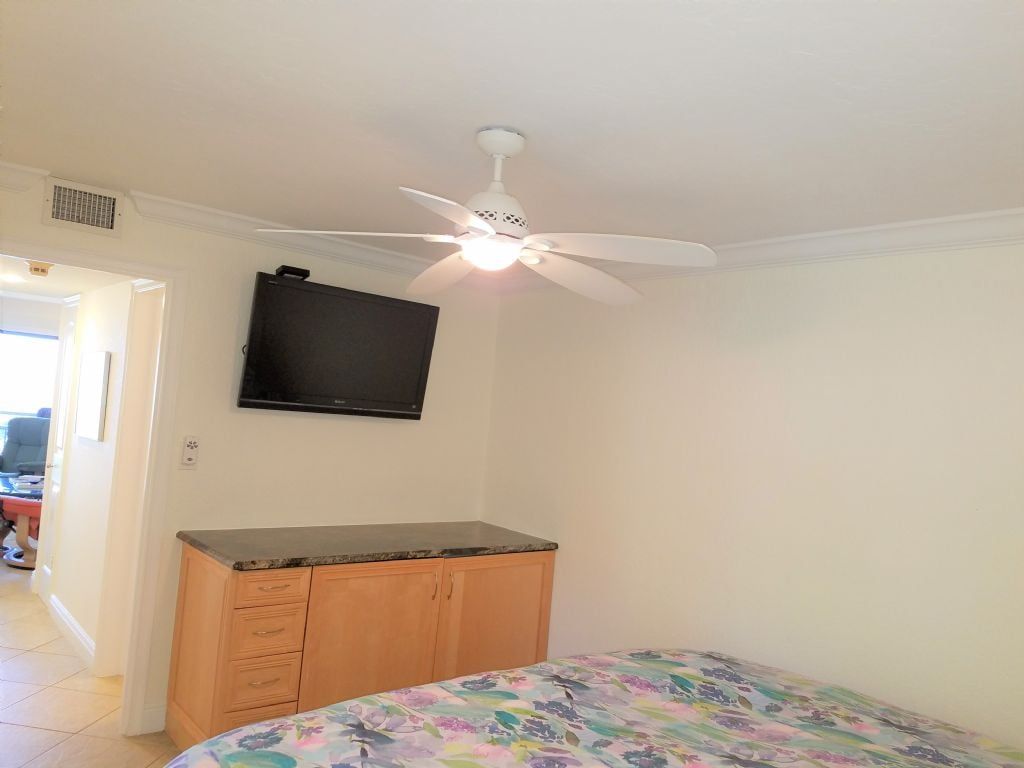 Une chambre à coucher comprenant un lit, un ventilateur de plafond, un téléviseur à écran plat et une armoire en bois.