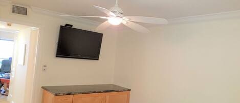 A bedroom with a bed, a ceiling fan, a flat-screen TV, and a wooden cabinet.