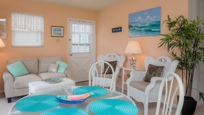 A living room with a beige sofa, white wicker chairs, a glass coffee table, and a potted plant. - 385 Cute 3 Bedroom Cottage in South Nags Head (Nags Head)