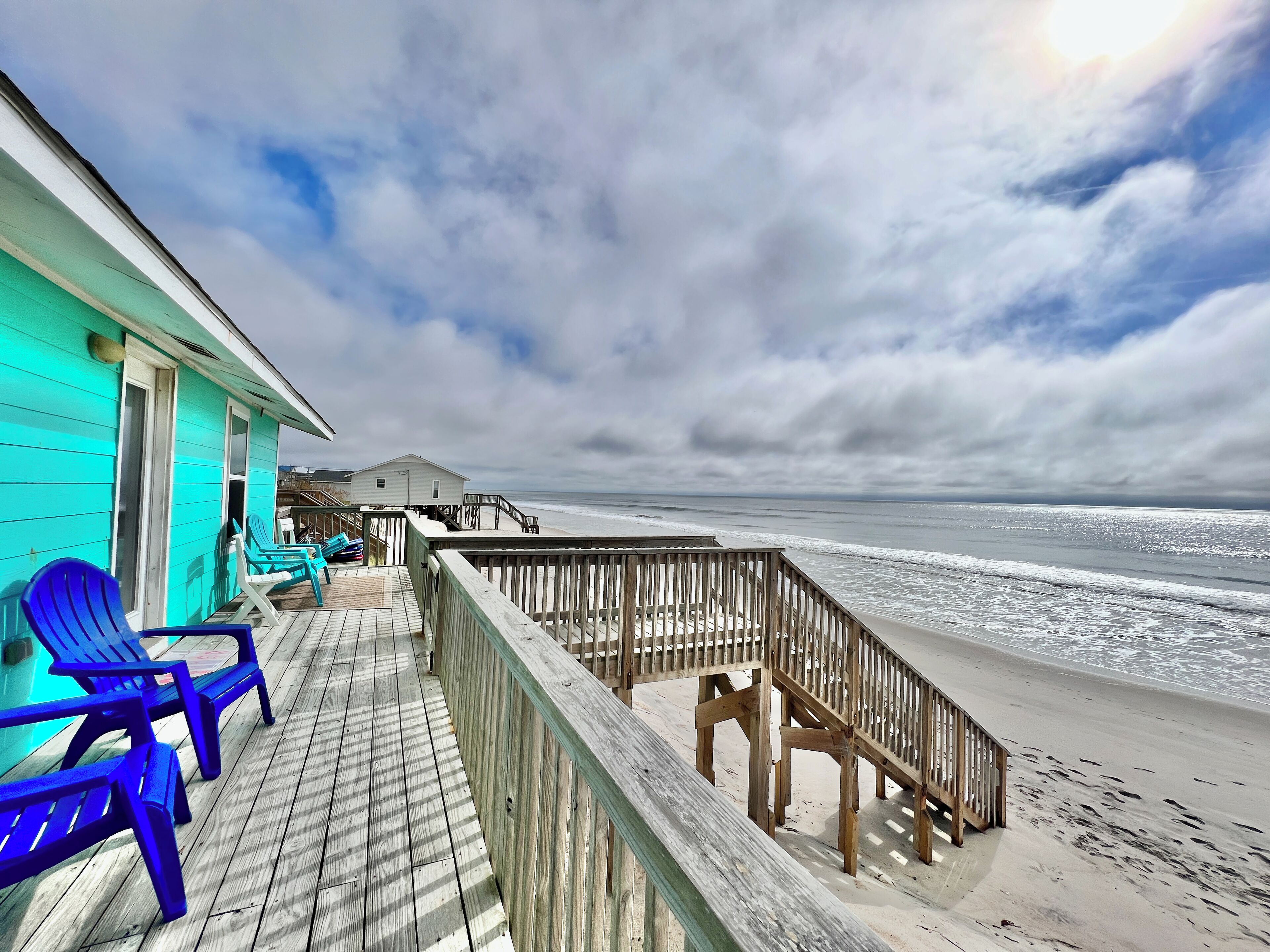 A wooden deck with blue chairs, a wooden railing, and a view of the ocean.