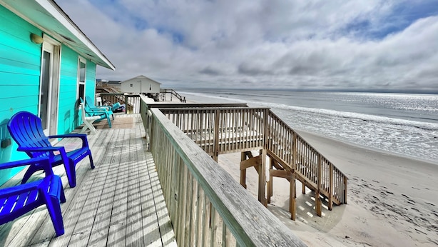 A wooden deck with blue chairs, a wooden railing, and a view of the ocean. - Riki Tiki | Oceanfront Home in Surf City (Surf City)