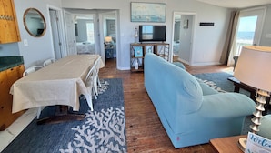 A room with a dining table, sofa, TV, and a view of the ocean. - Riki Tiki | Oceanfront Home in Surf City (Surf City)