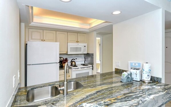 A modern kitchen with a granite countertop, stainless steel sink, white cabinets, a microwave, and a stove.