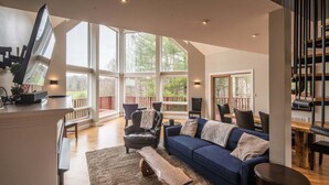 A spacious living area with a large window, a dark blue sofa, a wooden coffee table, and a black leather armchair.