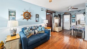 A living room with a blue sofa, wooden floors, a ceiling fan, and nautical-themed decorations. - 275 Unique Water-Front Home w/ Private Pier (Nags Head)