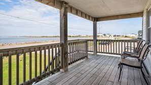 A wooden deck with a railing overlooking a body of water and a distant shoreline. - 275 Unique Water-Front Home w/ Private Pier (Nags Head)