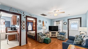 A living room with a wooden floor, a ceiling fan, a television, and a sofa. - 275 Unique Water-Front Home w/ Private Pier (Nags Head)