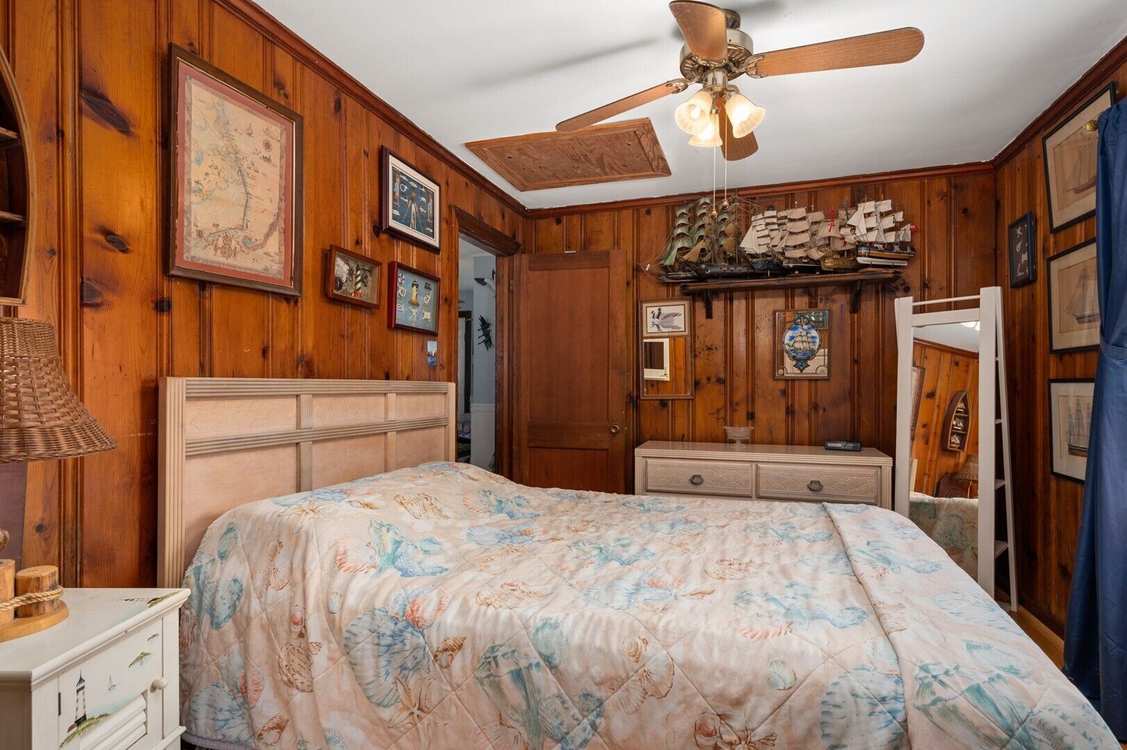 Una camera da letto con pannelli in legno, un letto con copripiumino floreale, una ventola a soffitto e un comò con specchio.