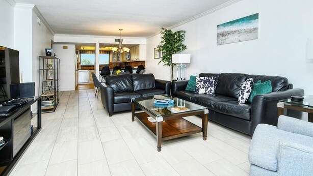 A modern living room with a black leather sofa, a glass coffee table, and a grey armchair. A television is on a stand to the left, and a plant is in the corner. - Chinaberry 932- 2 bedroom 2 full bath unit on 3rd floor overlooking bay (Siesta Key)