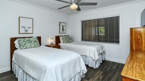 Ein Schlafzimmer mit zwei Betten, einem Deckenventilator, einem Fenster mit Jalousien und einem Holzschrank.