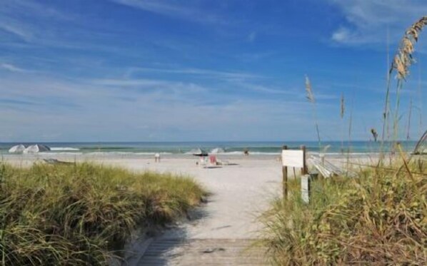 A sandy beach path leading to the sea with a clear sky.