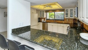 Eine Küche mit weißen Schränken, einer Granit Arbeitsplatte und einem Fenster mit Jalousien.