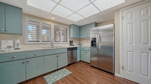 Eine moderne Küche mit türkisfarbenen Schränken, einem Edelstahlkühlschrank und einem Fenster mit Jalousien.
