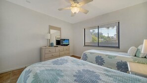 A bedroom with two beds, a dresser, a TV, and a ceiling fan.