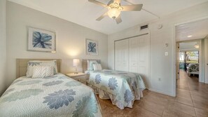 Ein Schlafzimmer mit zwei Betten, einem Deckenventilator und einer Tür zu einem anderen Raum.