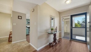 A hallway with a wooden floor, a glass door leading to a balcony, and a kitchen area in the background.