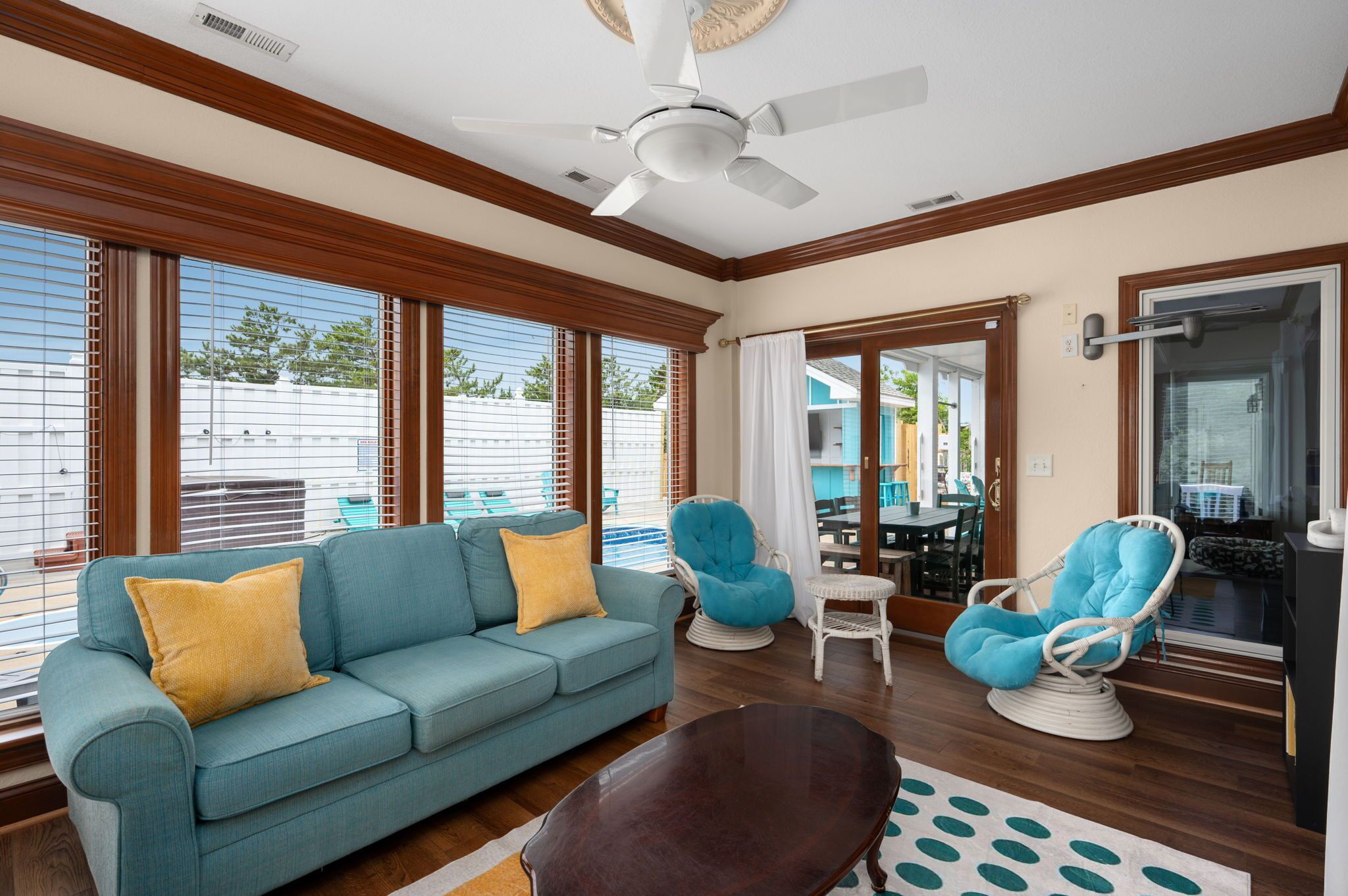 A living room with a sofa, two chairs, a ceiling fan, and large windows.