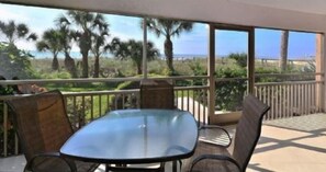 Un balcón con mesa y sillas, con vista a una playa y palmeras.