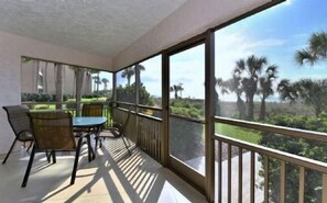 A balcony with a table and chairs, overlooking a landscape with palm trees. - Firethorn 110- Absolutely gorgeous, beachfront 2BR/2BA condo (Siesta Key)