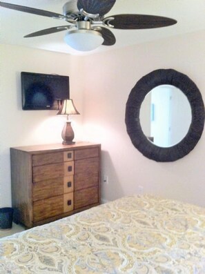 A bedroom with a bed, a dresser, a ceiling fan, a television, and a mirror.