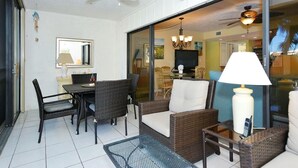 Un patio ensoleillé, aménagé avec des meubles en osier, une table à manger et un téléviseur en arrière-plan.