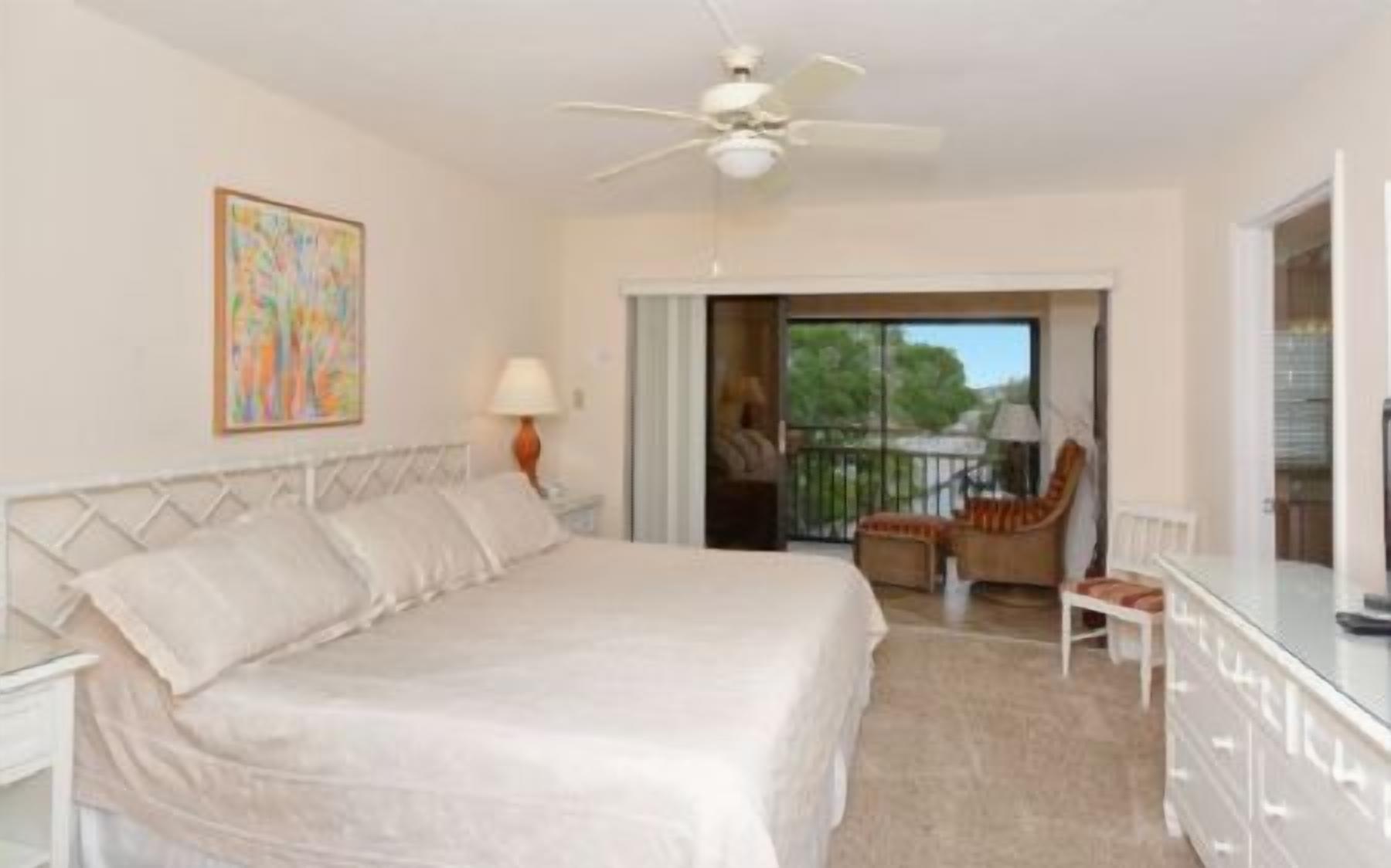 A bedroom with a bed, a chair, a desk, and a balcony with a view.