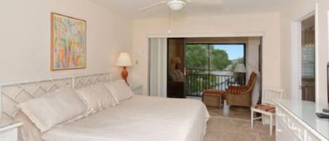 A bedroom with a bed, a chair, a desk, and a balcony with a view.