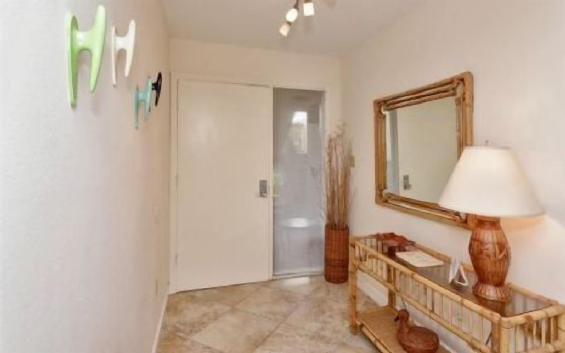 A hallway with a door, a mirror, a lamp, and a small table with a vase.