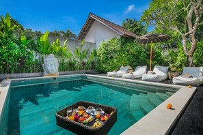 A pool area with a dining setup, lounge chairs, and a statue.
