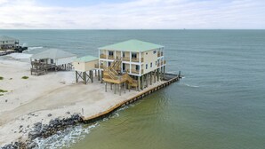 A beachfront property with a multi-level house on stilts, a covered deck, and a pier extending into the water. - Shamrock Shores - Gulf-front 6 Bedroom Beach House, 2 kitchens, Pet-Friendly (Dauphin Island)