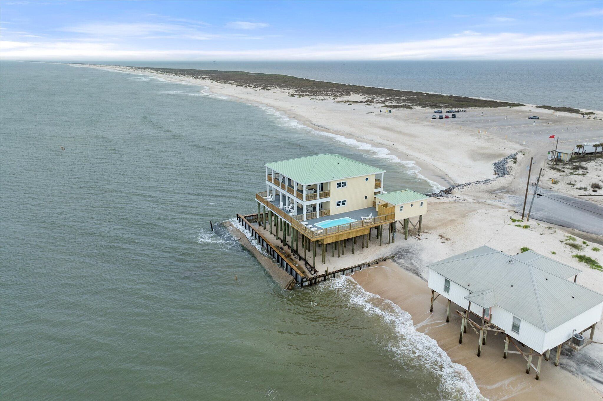 Une propriété située en bord de mer, avec un grand bâtiment doté de nombreux balcons, d’une piscine et d’une jetée s’avançant dans l’océan.