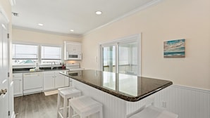 A kitchen with white cabinetry, a granite countertop, and a large island with bar stools. - Shamrock Shores - Gulf-front 6 Bedroom Beach House, 2 kitchens, Pet-Friendly (Dauphin Island)
