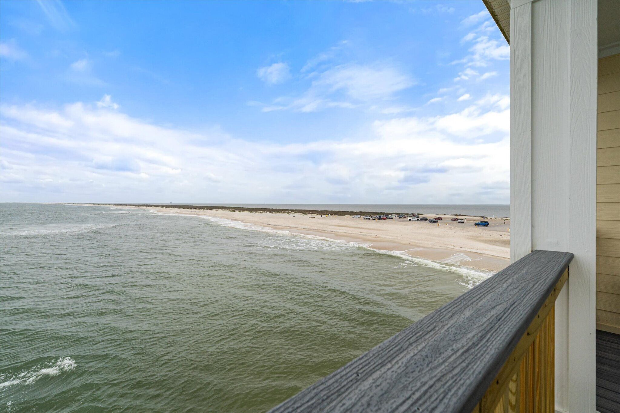 A beach view from a wooden balcony with a railing.