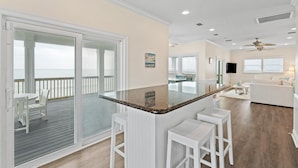 A spacious kitchen with a large island, sliding glass doors leading to a balcony, and a living area with a sofa and TV. - Shamrock Shores - Gulf-front 6 Bedroom Beach House, 2 kitchens, Pet-Friendly (Dauphin Island)