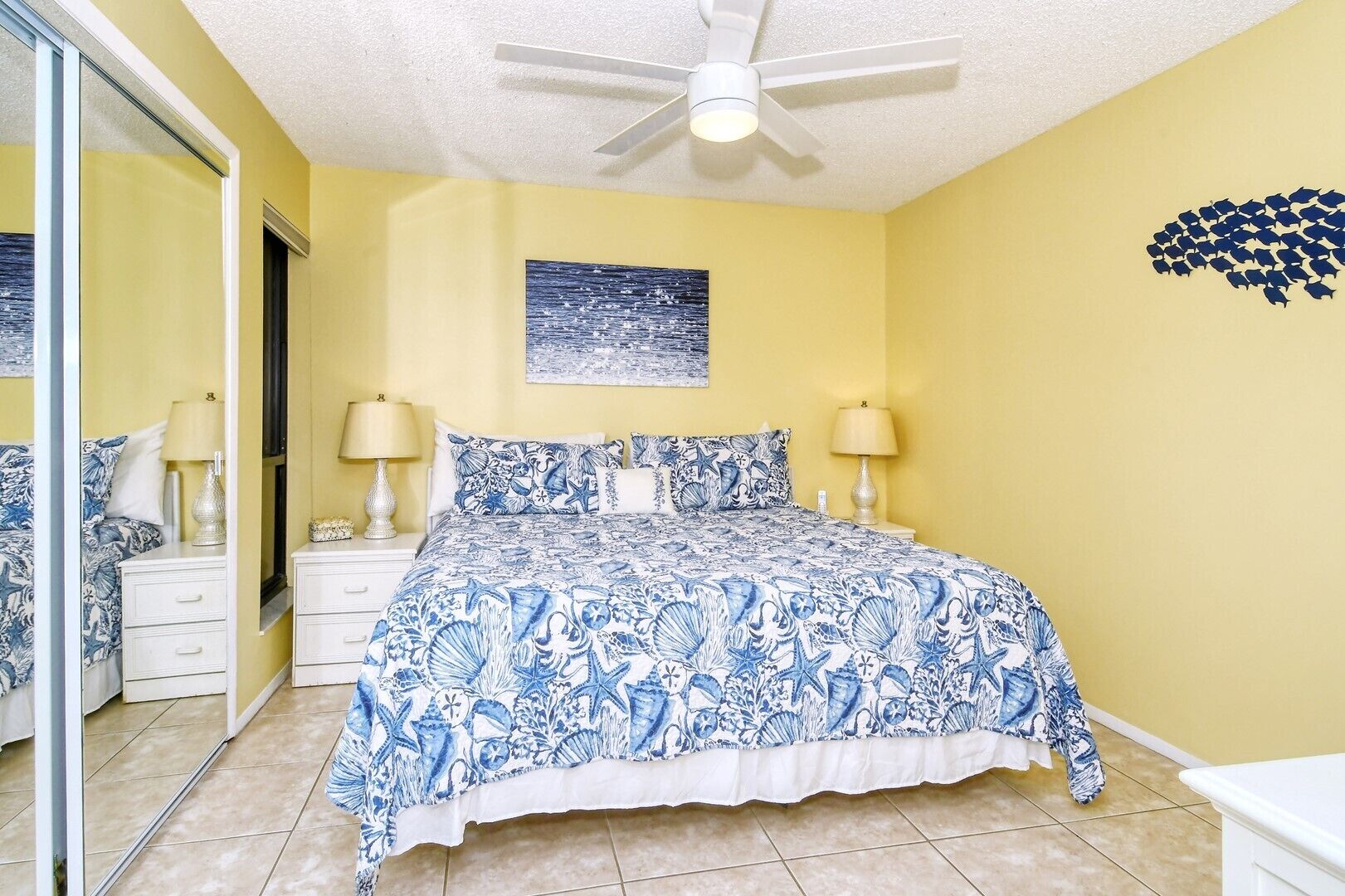 A bedroom with a bed, two bedside tables, a ceiling fan, and a wall with a framed picture.