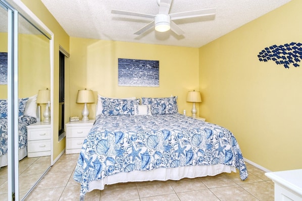 A bedroom with a bed, two bedside tables, a ceiling fan, and a wall with a framed picture.
