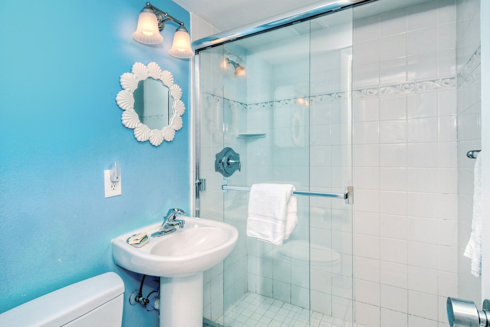 A bathroom with a sink, mirror, and glass shower enclosure.