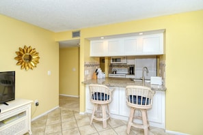 A compact kitchen with white cabinets, a microwave, and a toaster. There are two wicker bar stools with cushions.