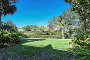 A well-maintained grassy area with a wooden fence, surrounded by various trees and shrubs.