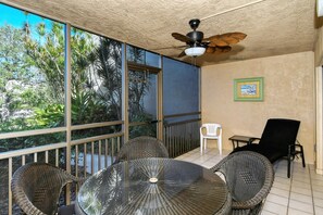 Ein Balkon mit Tisch und Stühlen, einem Deckenventilator und Blick ins Grüne.