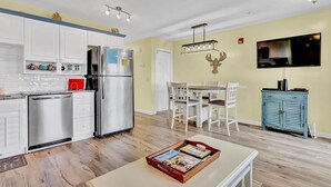 A modern kitchen with white cabinets, stainless steel appliances, and a dining area with a white table and chairs. - Sea Coast Suites 10 | Surf City, NC | Elevator (Surf City)
